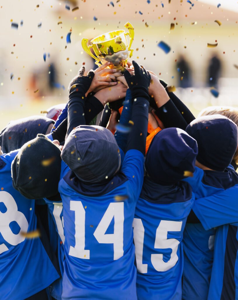 boys in blue winter soccer jersey shirts rising golden trophy at champions ceremony. kids in winter hats celebrating sports success in a team